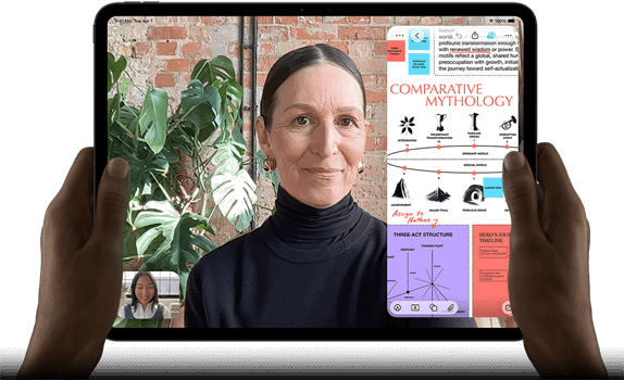 iPad Pro, front exterior, landscape orientation, space black colour, rounded corners, black display bezel, hands holding left and right sides, display showing a FaceTime conversation being live translated, and an educational app showing a presentation of Comparative Mythology with text, diagrams and handwritten notes